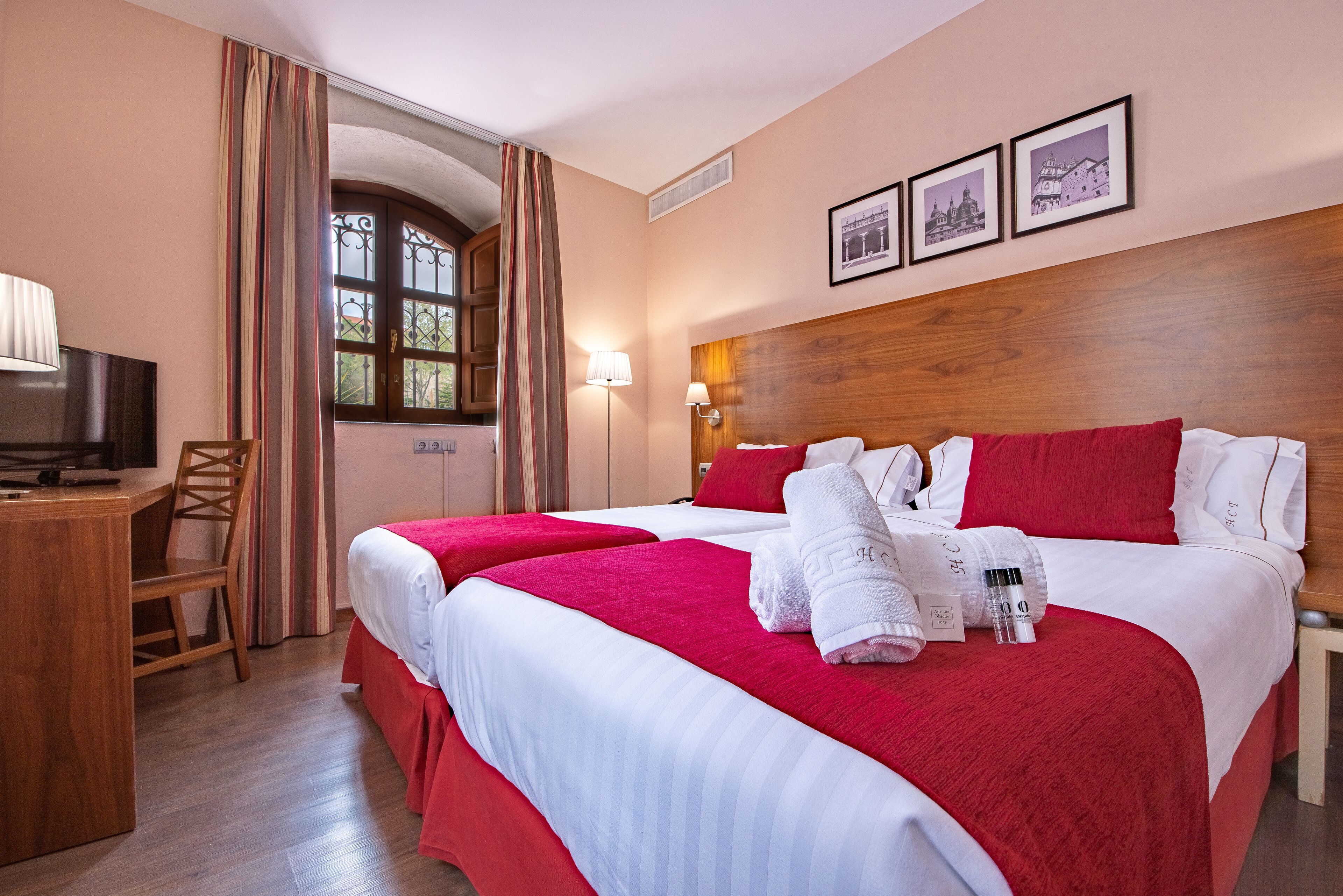 Habitación de hotel con dos camas, un escritorio, un televisor y una ventana con cortinas.