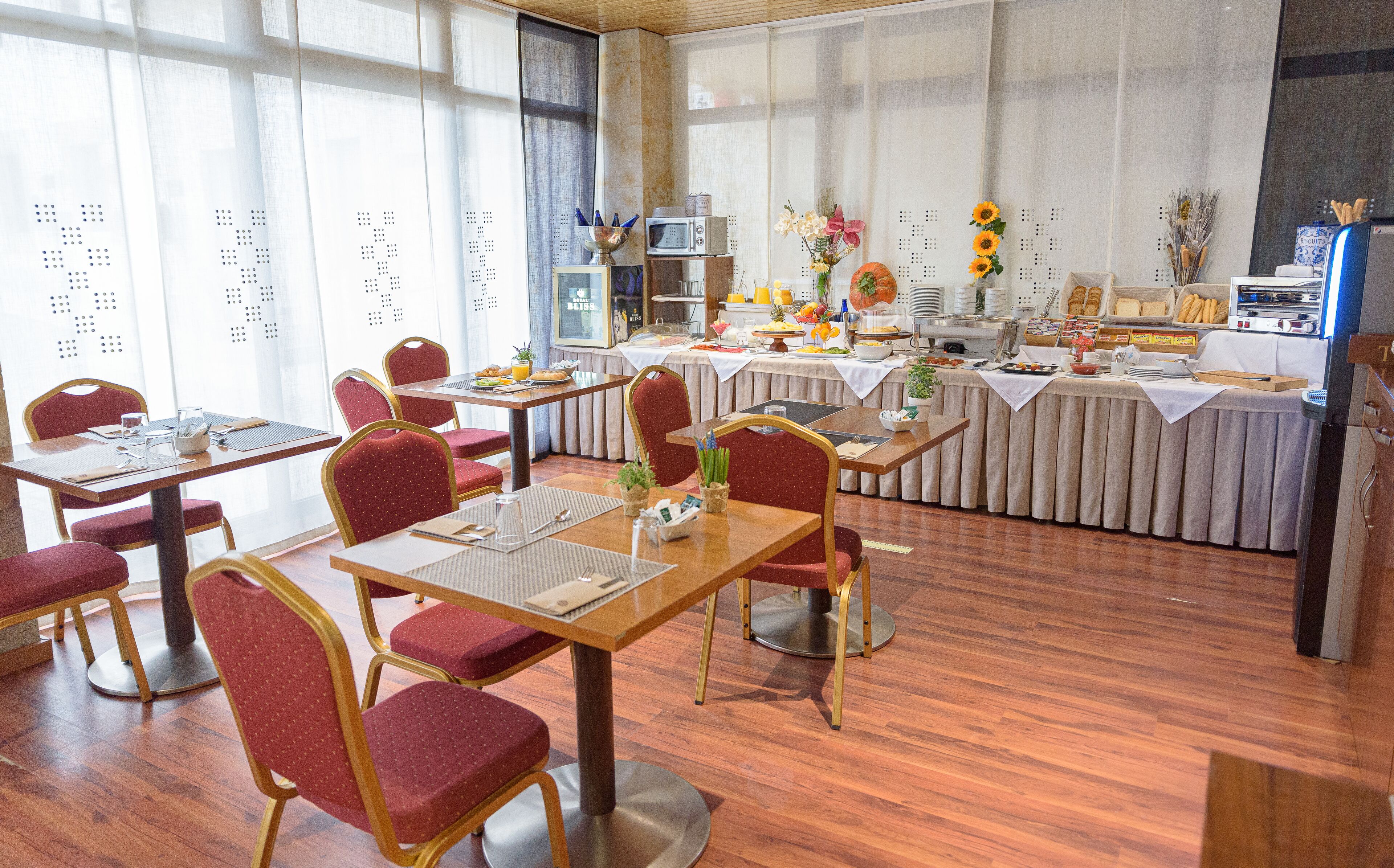A dining area with wooden tables and red upholstered chairs, a buffet with various food items, and a microwave on a counter.