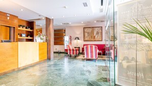 A hotel reception area with a wooden reception desk, a Coca-Cola refrigerator, a red sofa, and a glass partition. - Hospedium Hotel Casino del Tormes (Salamanca)