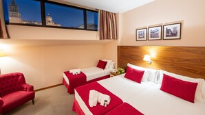 A hotel room with two beds, a red armchair, a nightstand with a lamp, and a window with a cityscape view. - Hospedium Hotel Casino del Tormes (Salamanca)