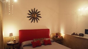 Une chambre d’hôtel avec une tête de lit rouge, un décor mural représentant un soleil, une table de chevet avec une lampe et une petite étagère avec quelques objets.