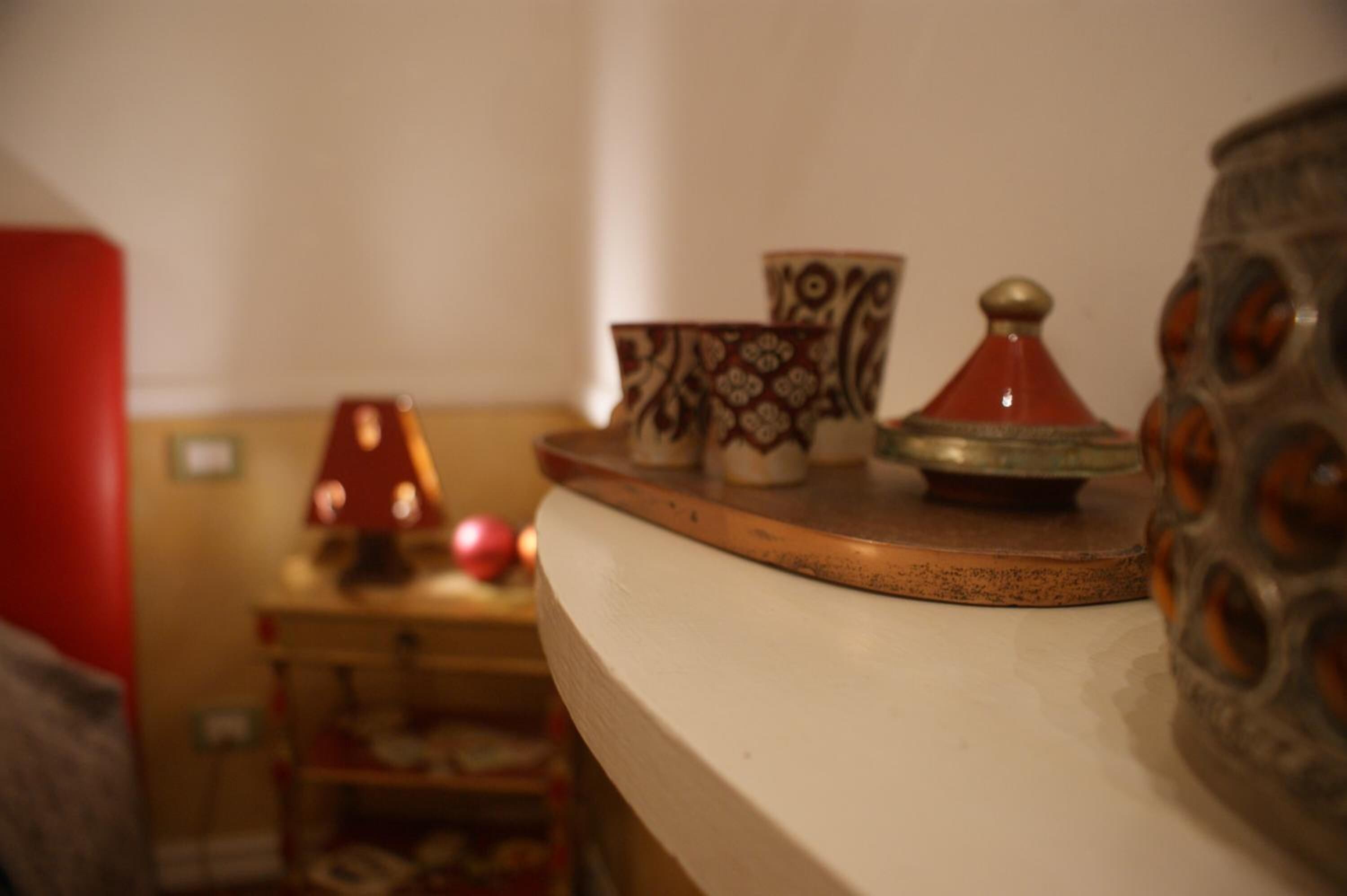 A table with decorative items including a patterned bowl, a red and gold container, and a metal vase.