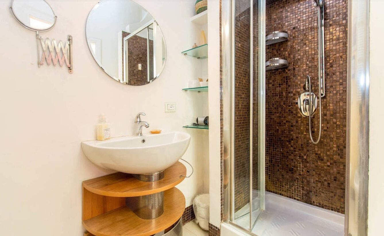 A bathroom with a large sink, two mirrors, a glass shower enclosure, and a tiled shower wall.