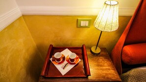 Une petite table d’appoint en bois, sur laquelle se trouve un plateau contenant deux tasses et leurs soucoupes, une boîte de mouchoirs et un interrupteur vert au mur.