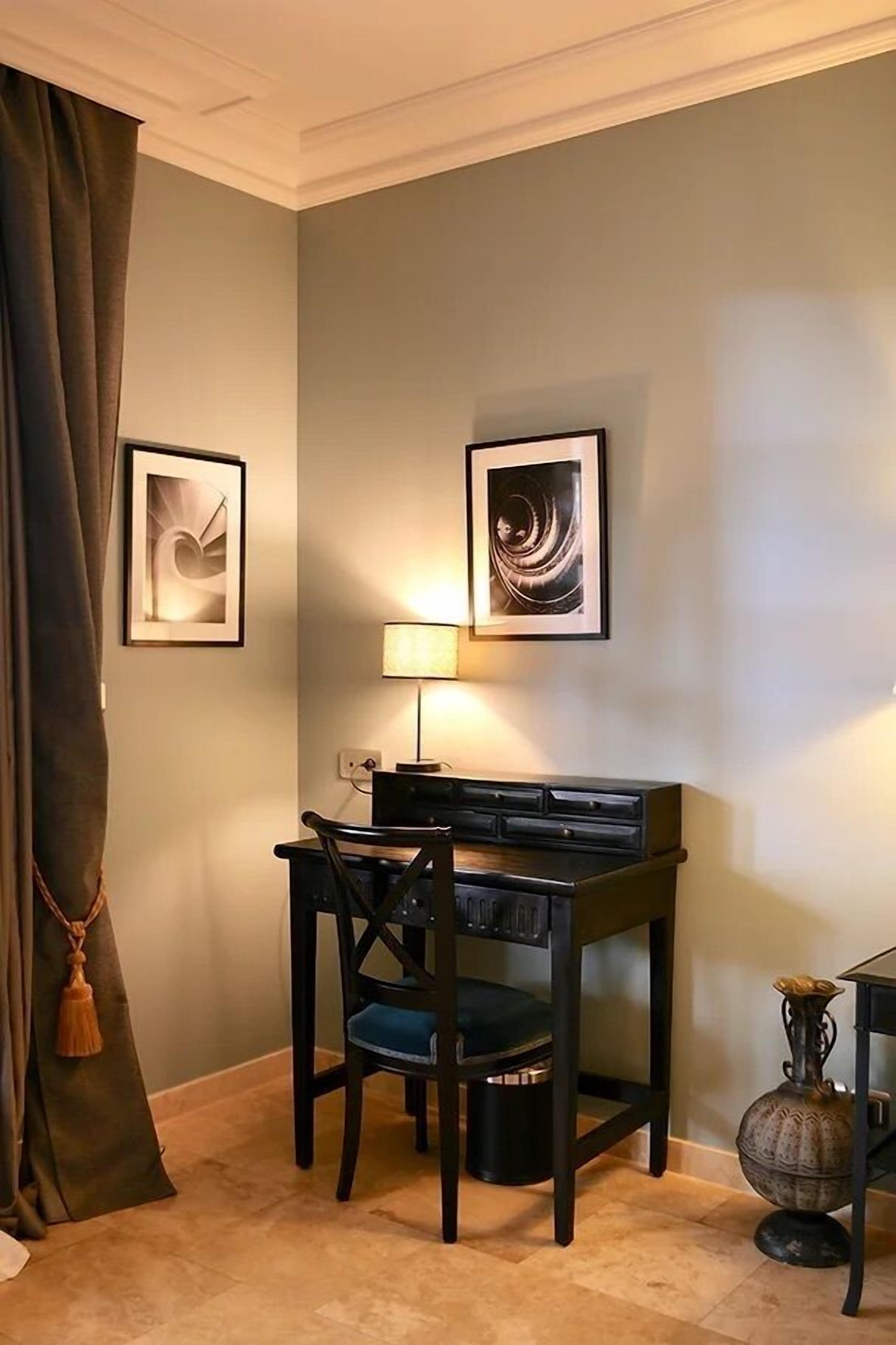 A dining area with a table, chairs, a lamp, and two framed artworks on the wall.