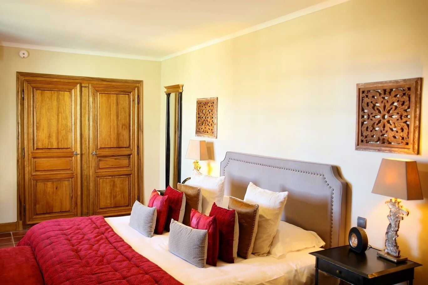 A hotel room with a large bed, a nightstand with a lamp, and a wardrobe.