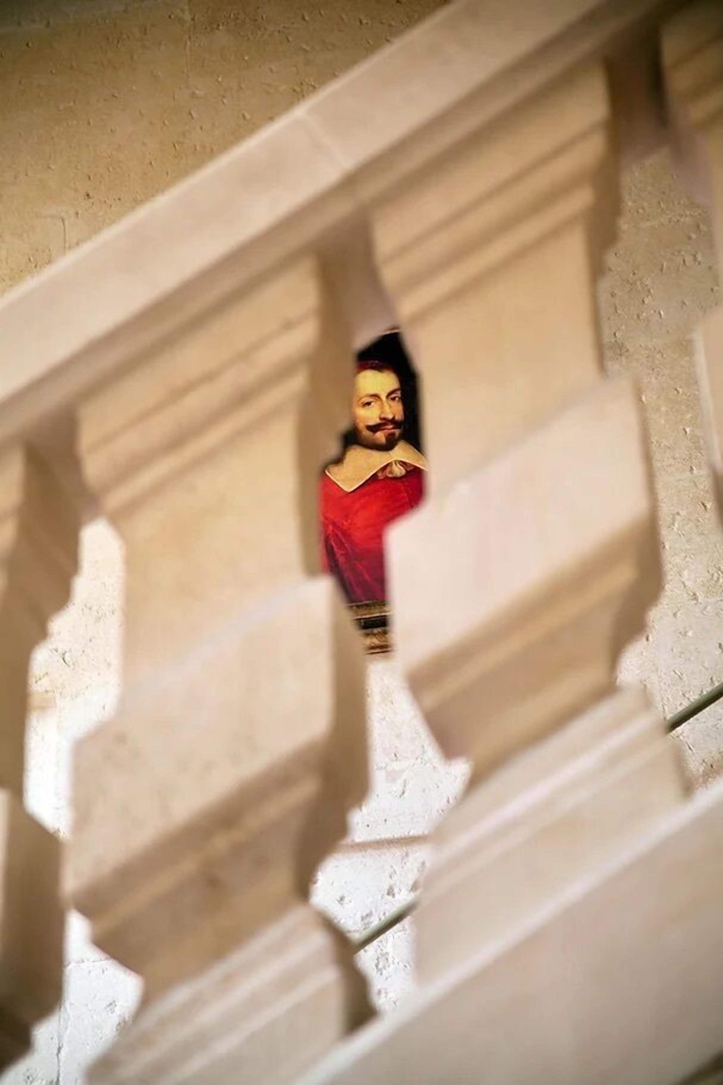 Estátua de uma pessoa vestida de vermelho, parcialmente escondida por elementos arquitetônicos.