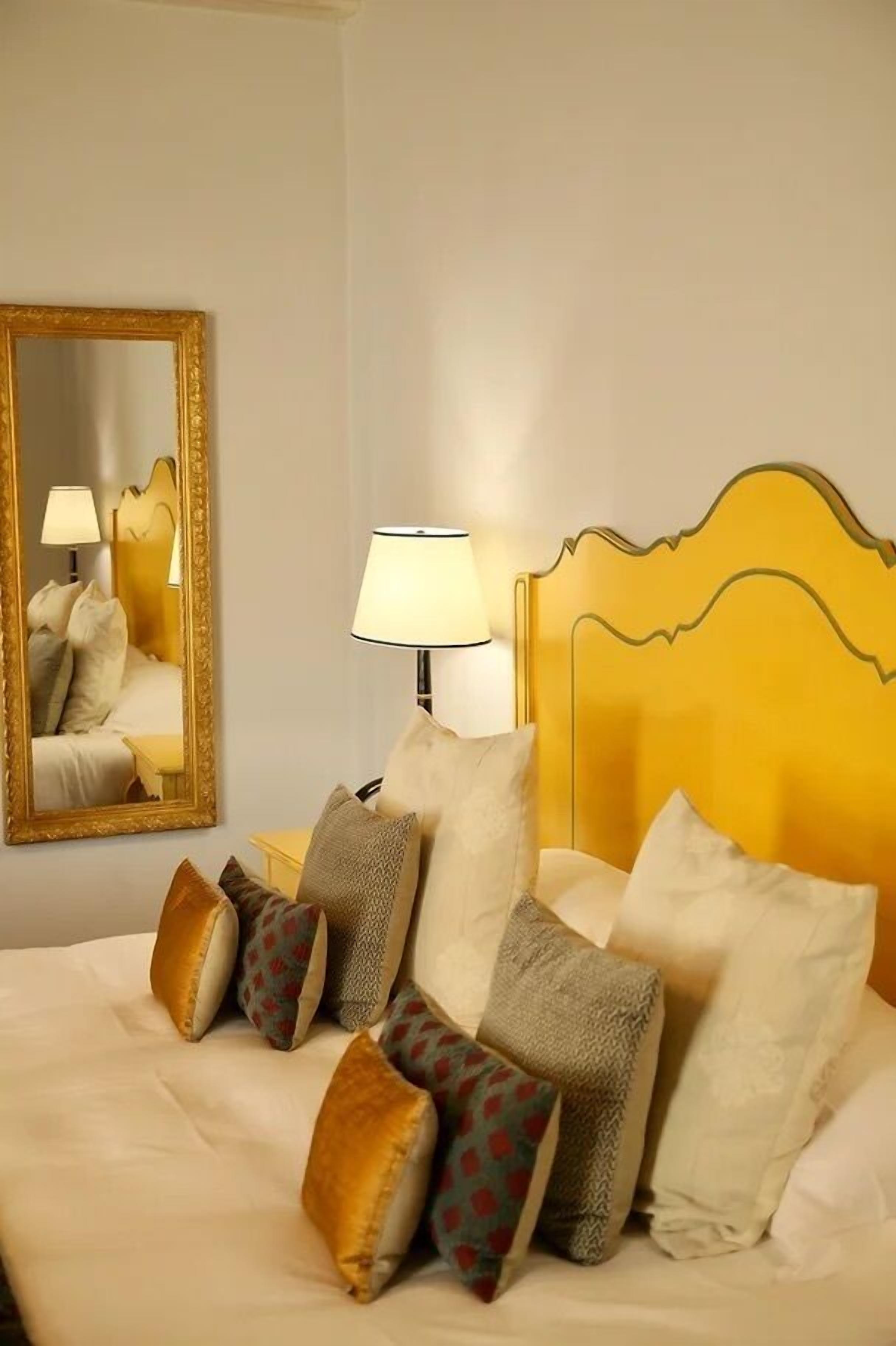 A hotel room with a bed, pillows, a mirror, and a lamp.