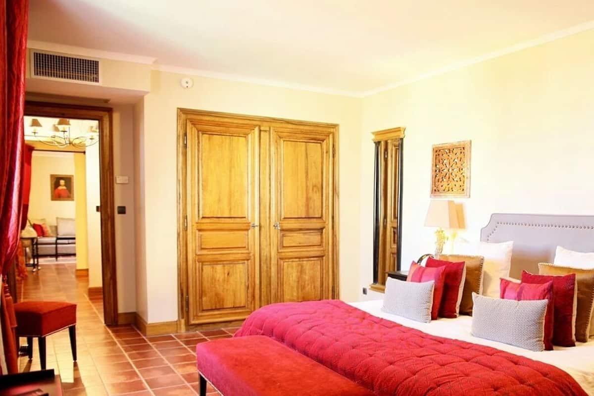 Een hotelkamer met een groot bed, een bankje, houten kasten en uitzicht op de gang.