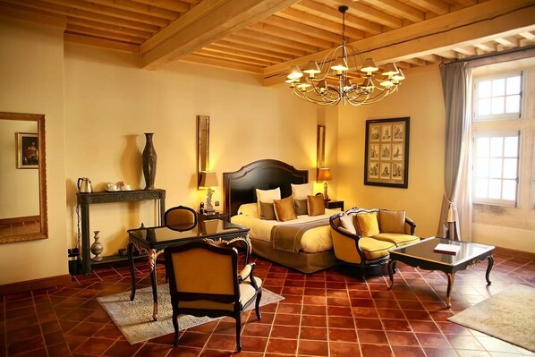 A hotel room with a bed, a sofa, a coffee table, a fireplace, and a chandelier. - Villa Mazarin Aigues Mortes (Aigues-Mortes)