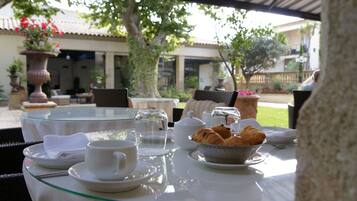 A table set for breakfast with croissants, a teapot, cups, and a bowl of fruit.