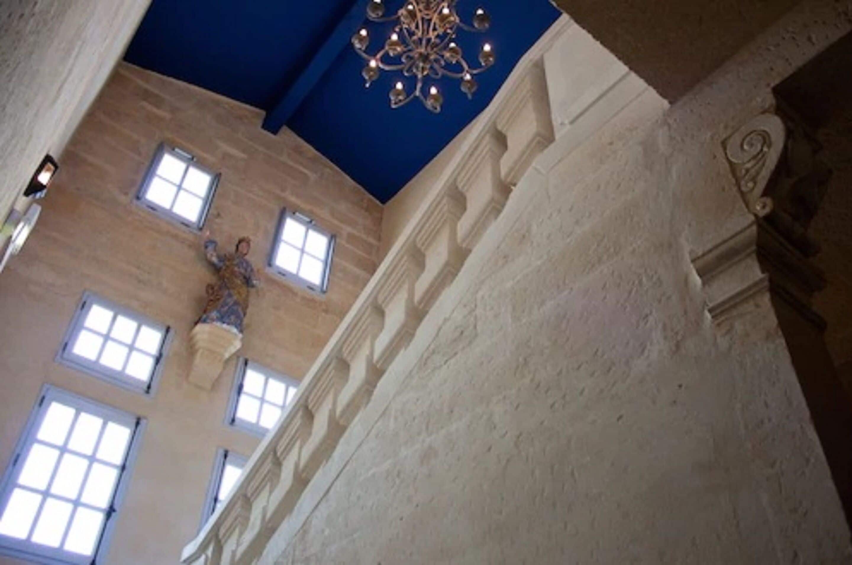 Un interior con techos altos, un candelabro, ventanas amplias y una pared de piedra.