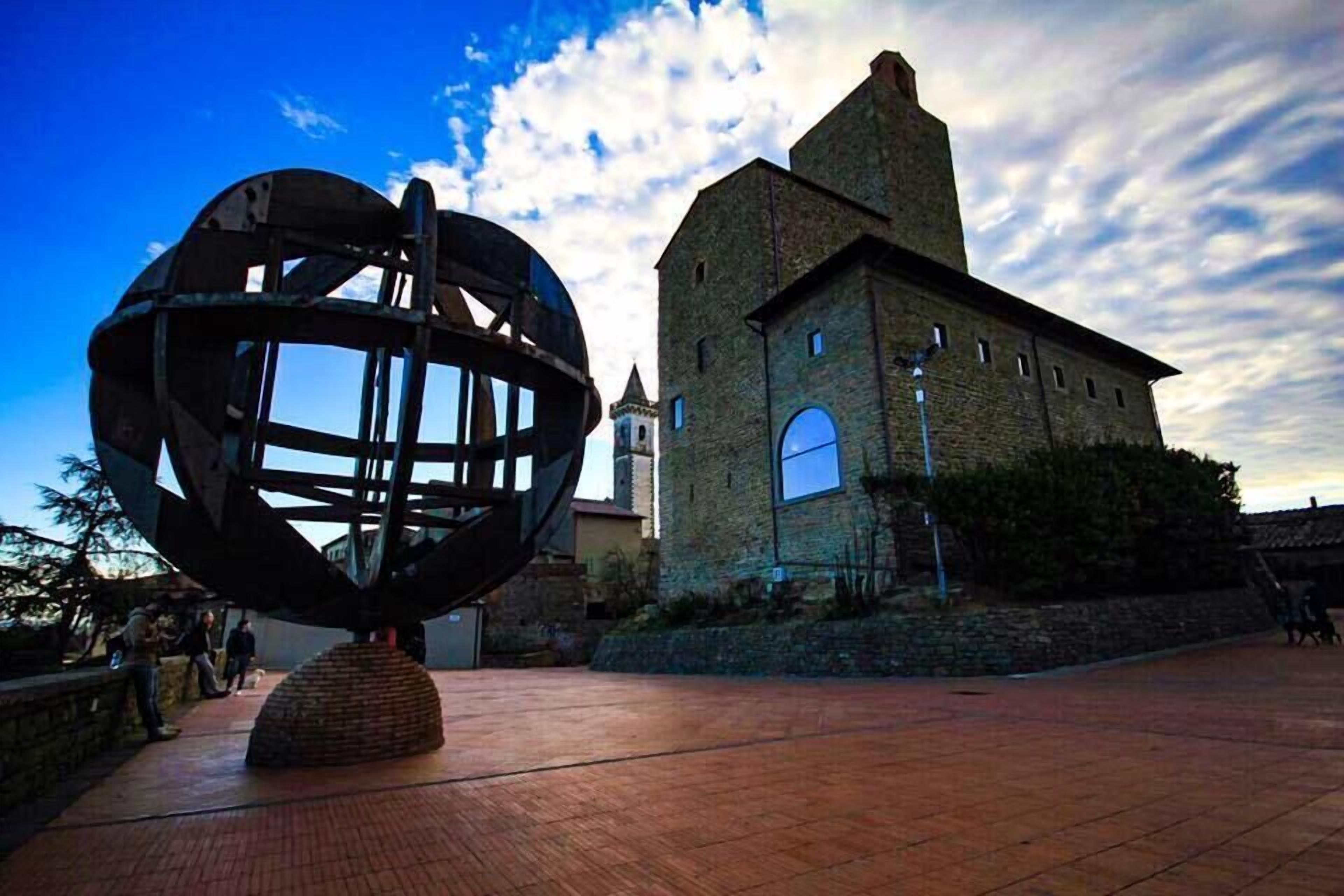 A historic building with a clock tower and a large metal sculpture in front.