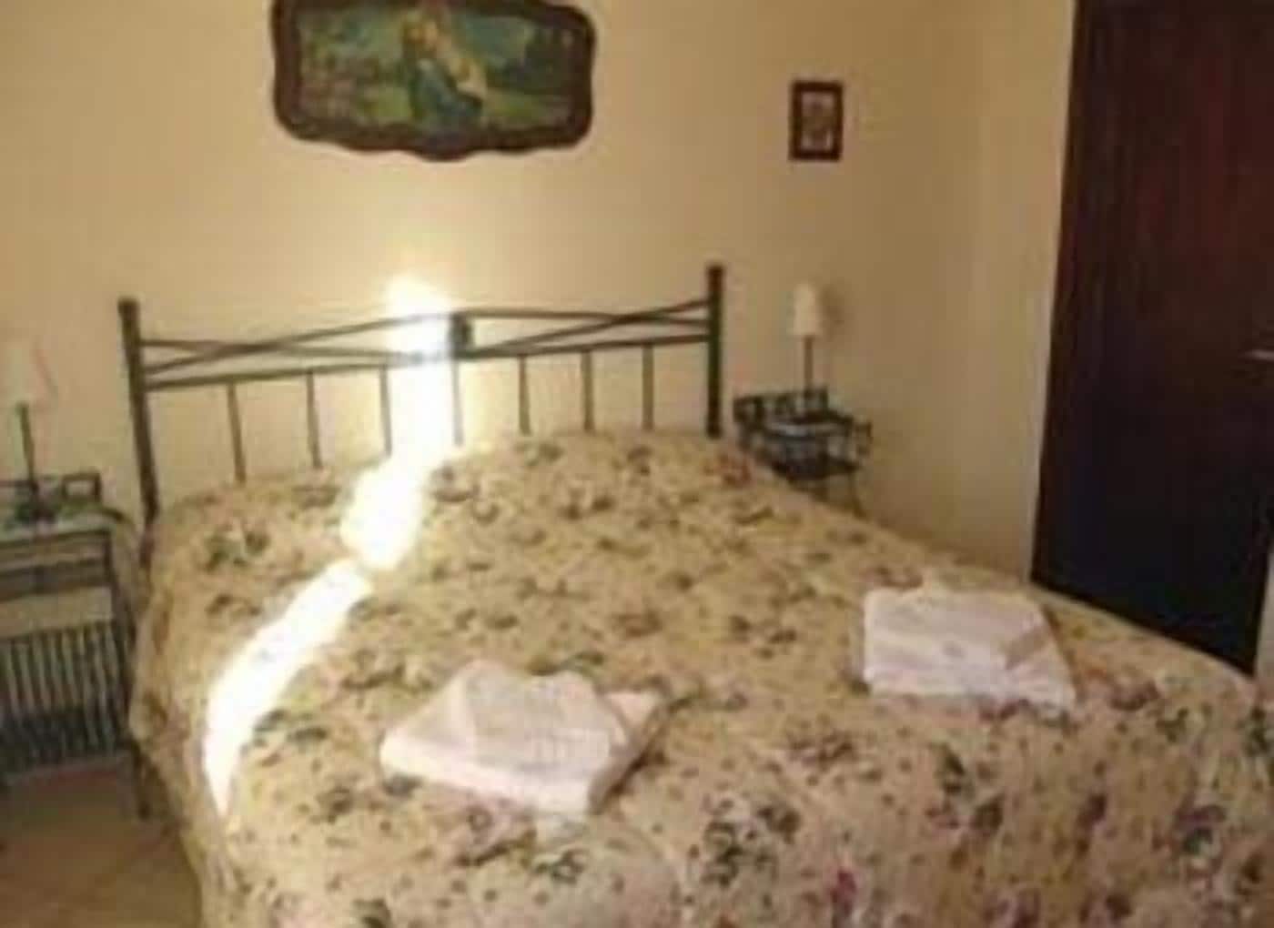A bedroom with a single bed, a nightstand, a lamp, and a painting on the wall.