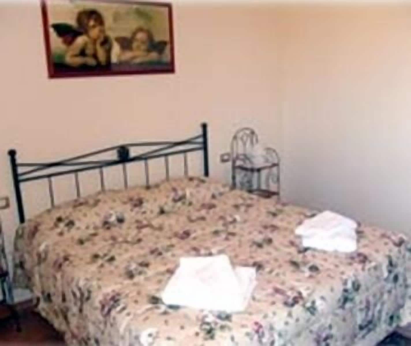 Un dormitorio con estructura de cama metálica, colcha estampada y una mesita de noche con lámpara.