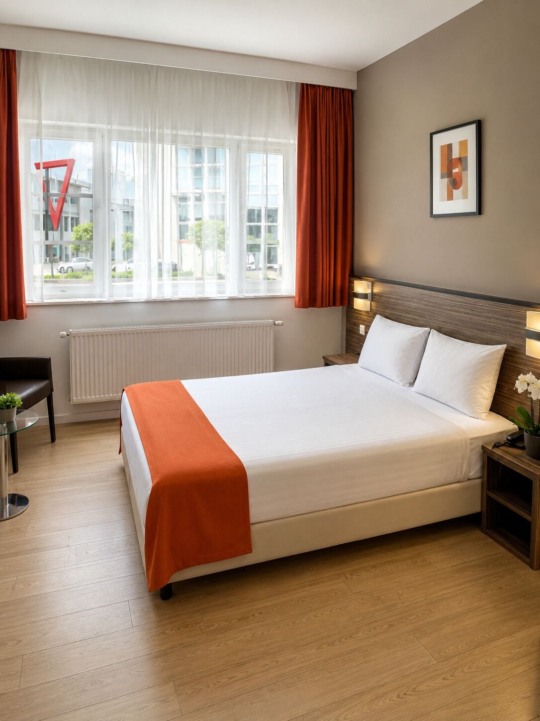 Una camera d'albergo con un letto grande, una scrivania, una sedia, un termosifone e una finestra con tende.