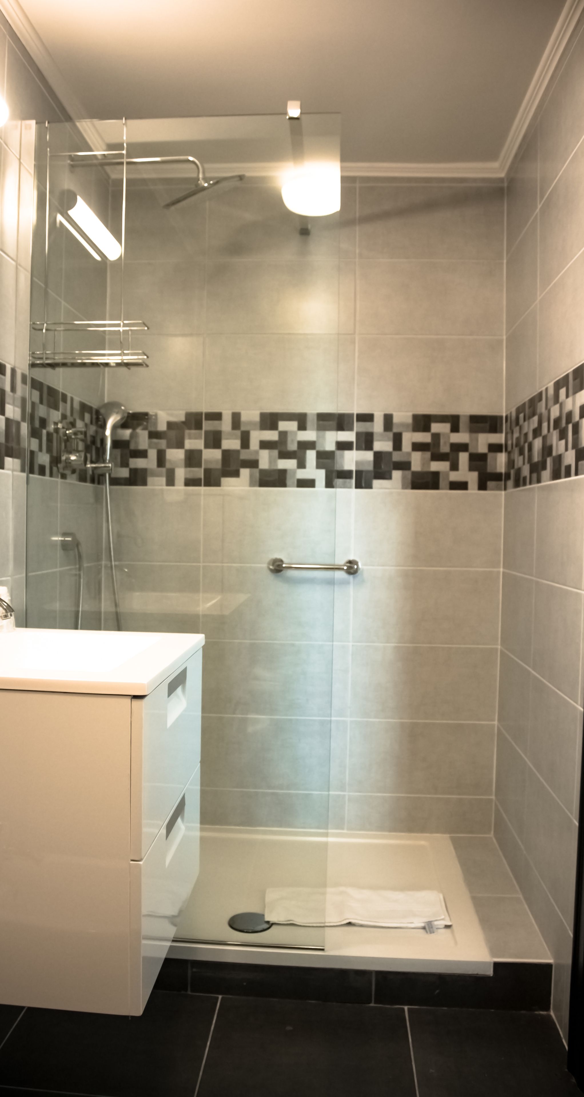 A modern bathroom with a glass-enclosed shower, a white vanity, and a tiled floor.