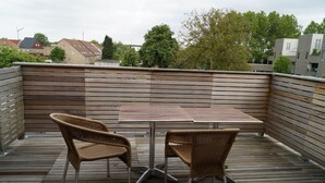 Una terraza de madera con una mesa y dos sillas de mimbre, rodeada por un cerco de madera.