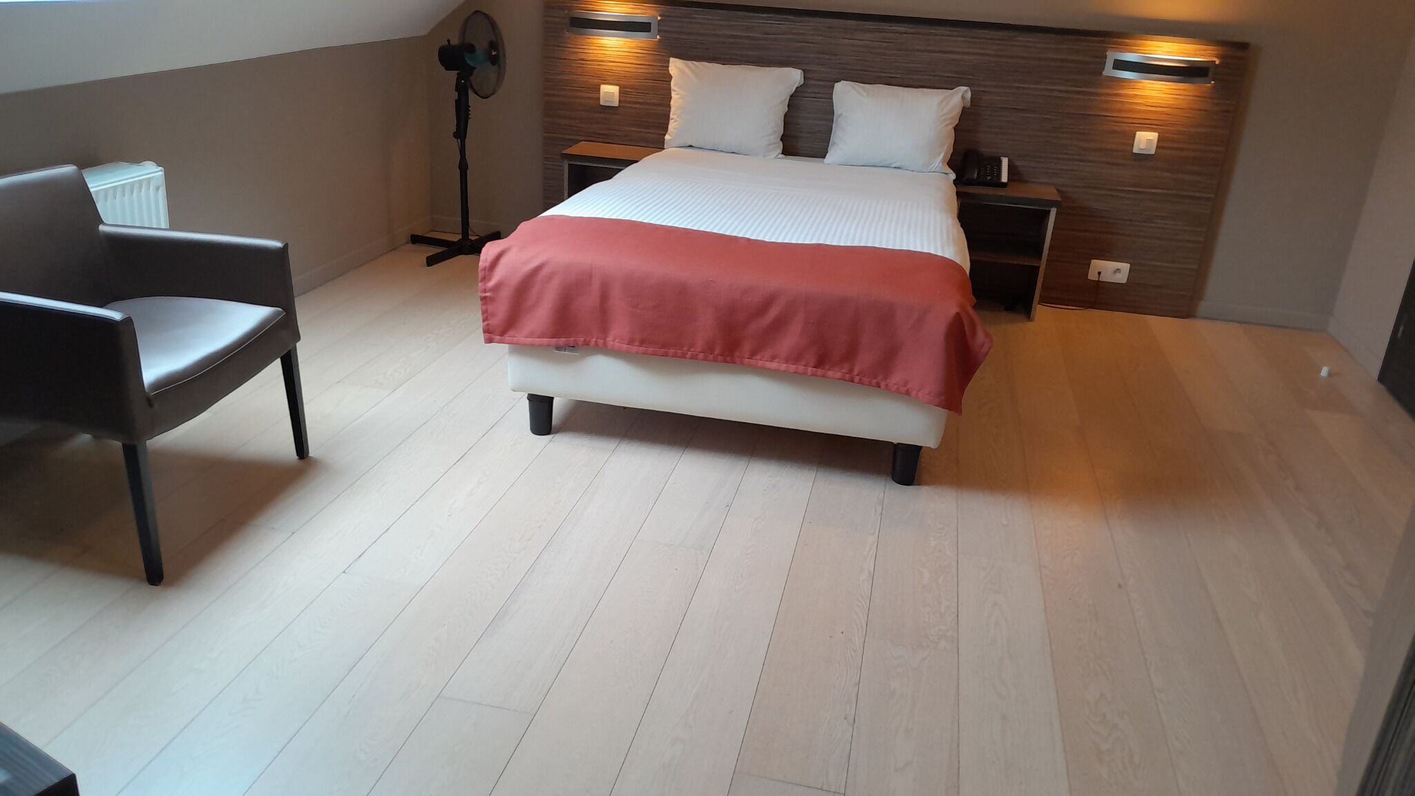 Ein modernes Schlafzimmer mit Bett, Nachttischen, einem Sessel und einem Standventilator.