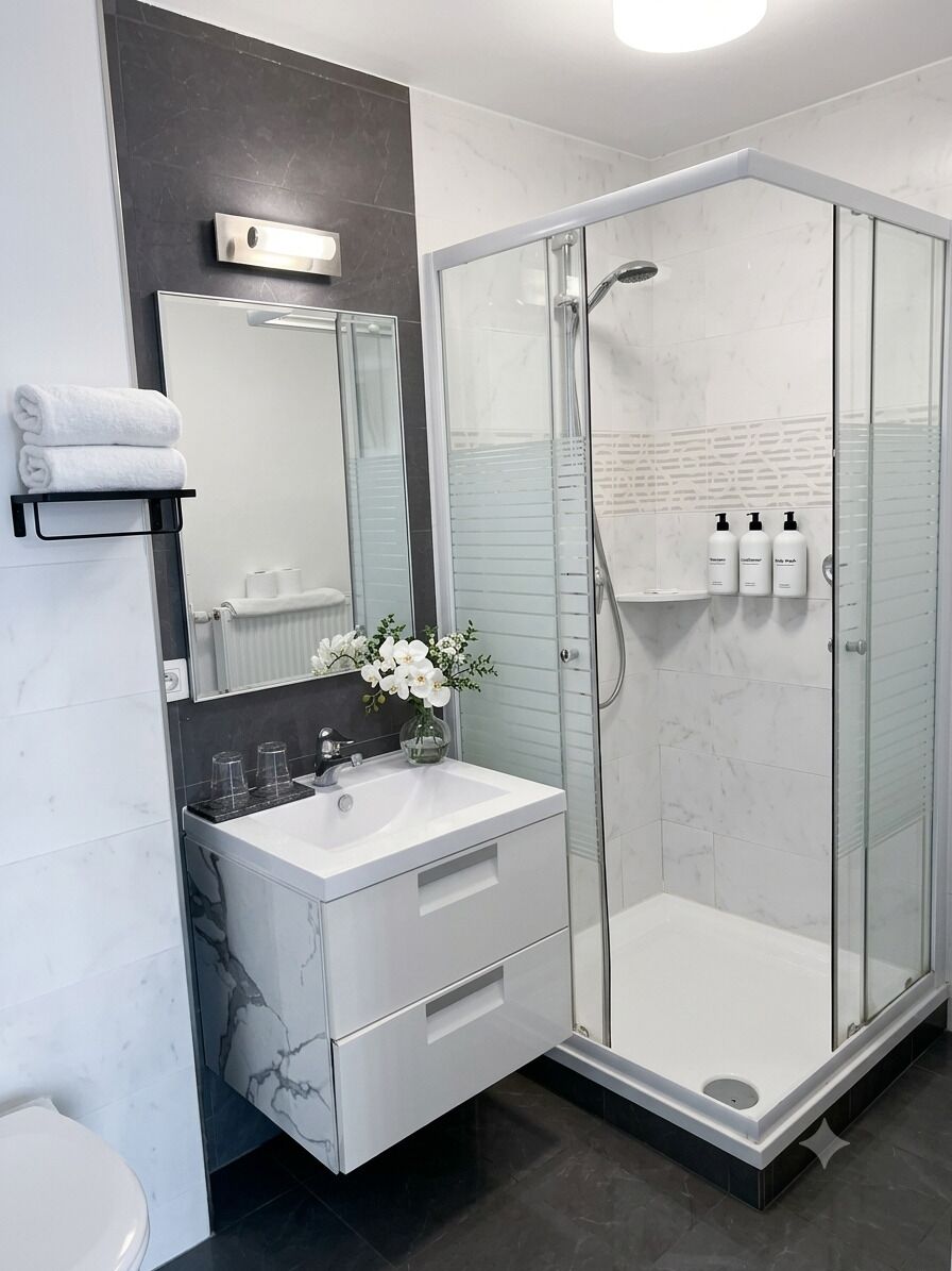 Un baño moderno con ducha de vidrio, un lavabo blanco con detalles de mármol y un espejo sobre el lavabo.