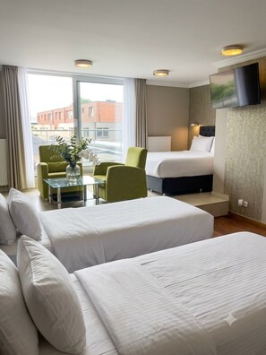 A hotel room with a bed, two chairs, a small table with a vase, and a TV mounted on the wall. - Hotel Taormina Brussels Airport (Zaventem)