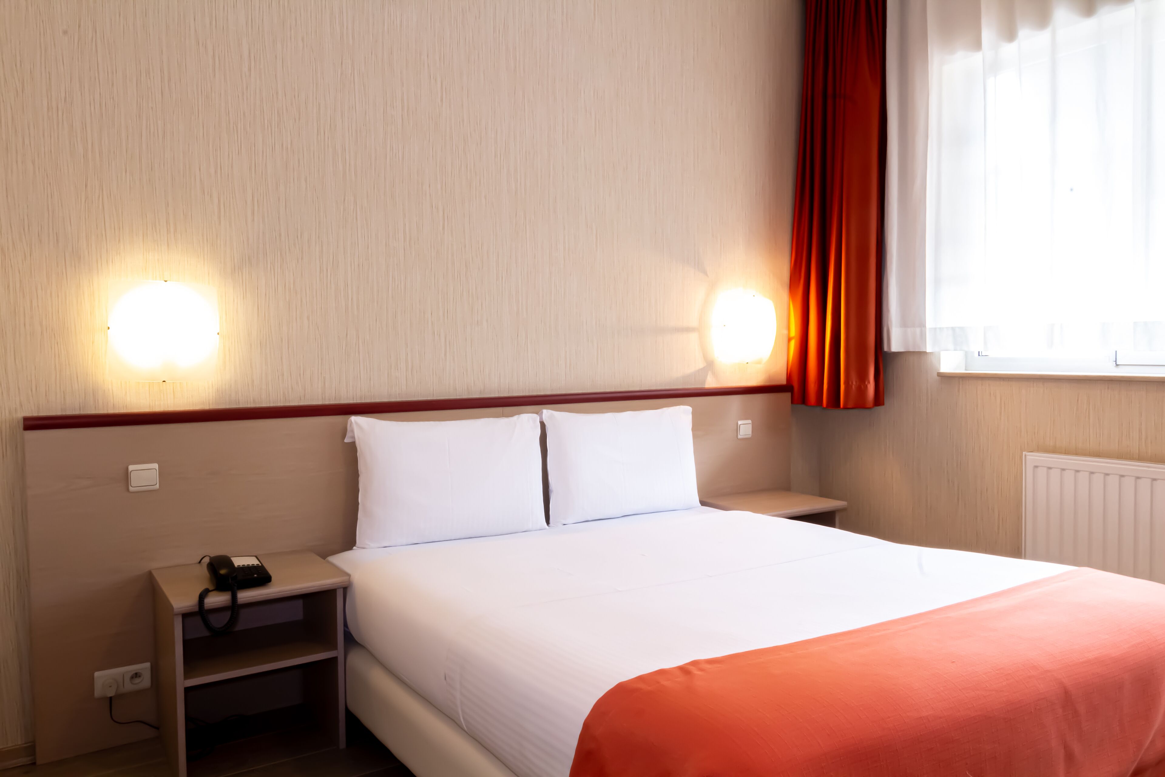 Habitación de hotel con cama, dos mesitas de noche, un teléfono y una ventana con cortinas.