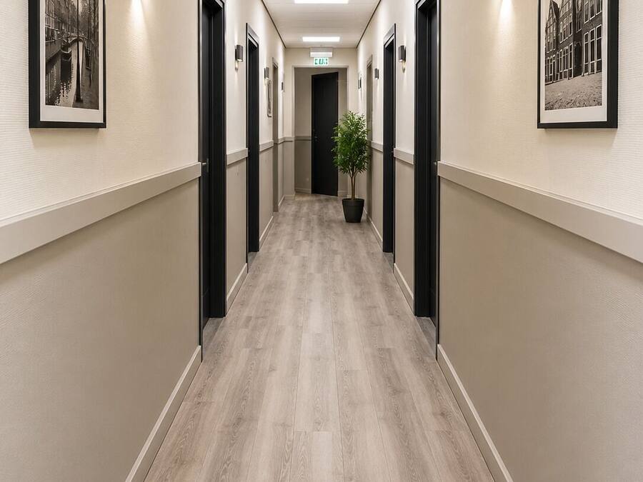 Un pasillo con fotografías blanco y negro enmarcadas en las paredes, una planta en maceta y una puerta al final.