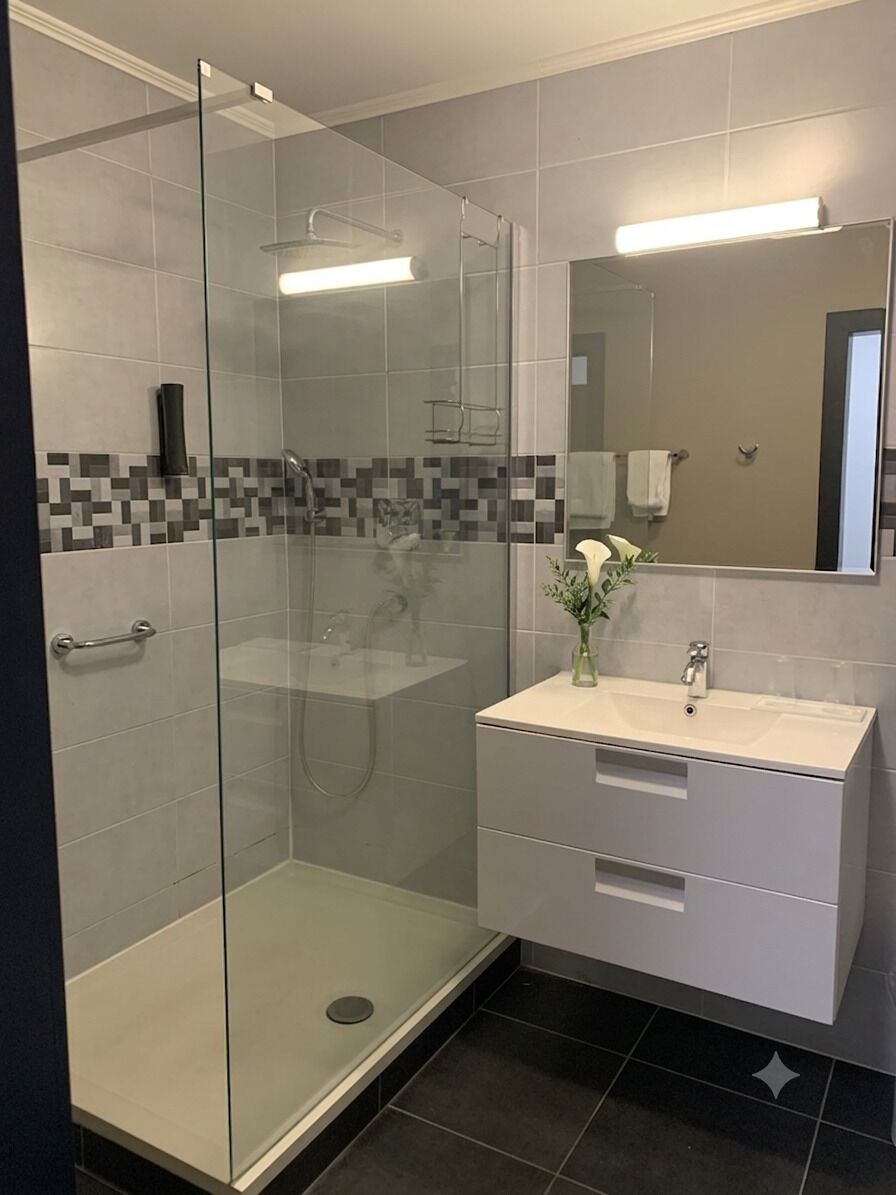 A modern bathroom with a glass-enclosed shower, a vanity with a mirror, and a tiled backsplash.