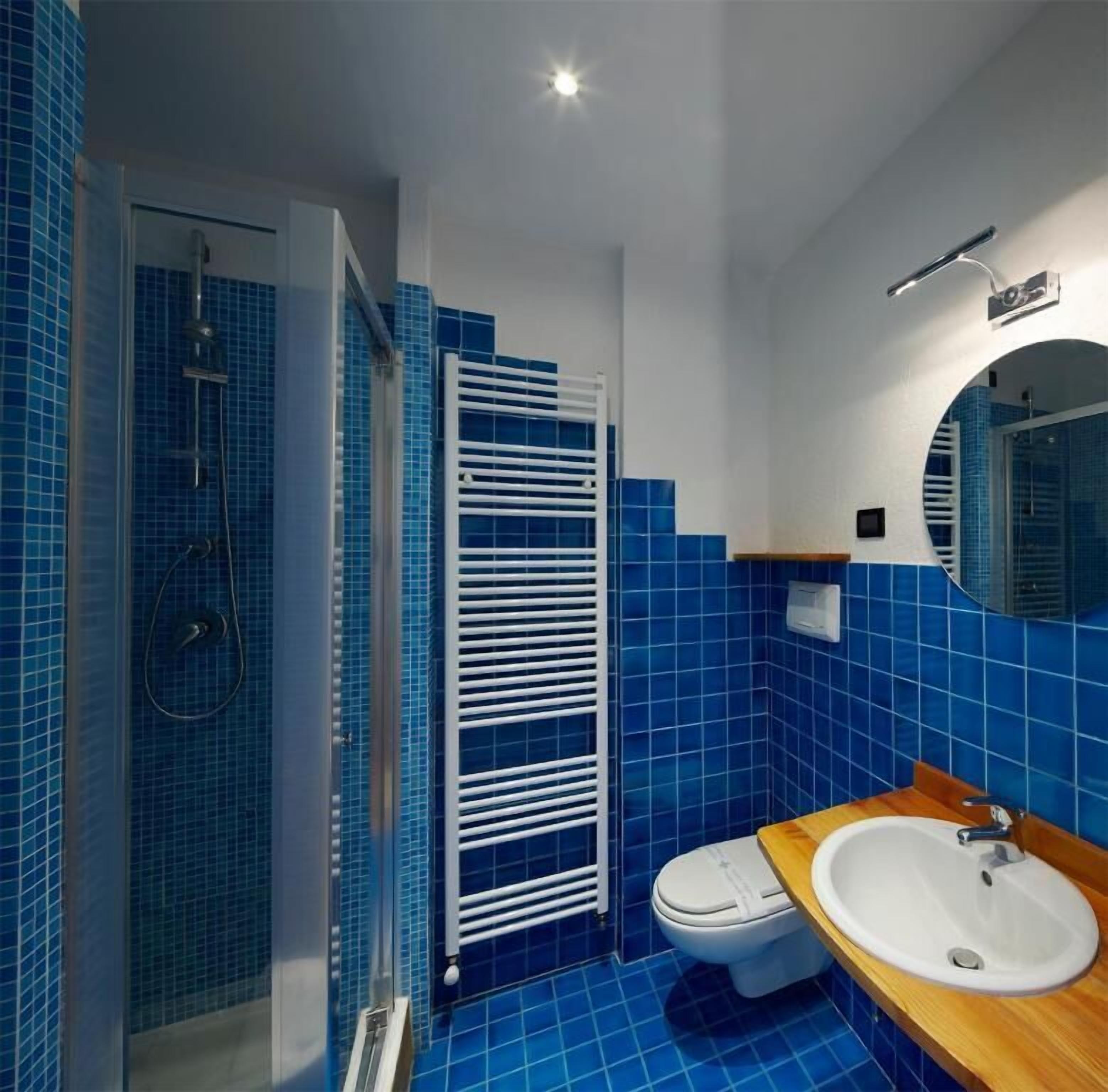 A bathroom with blue tiles, a white toilet, a wooden vanity with a sink, and a glass shower enclosure.