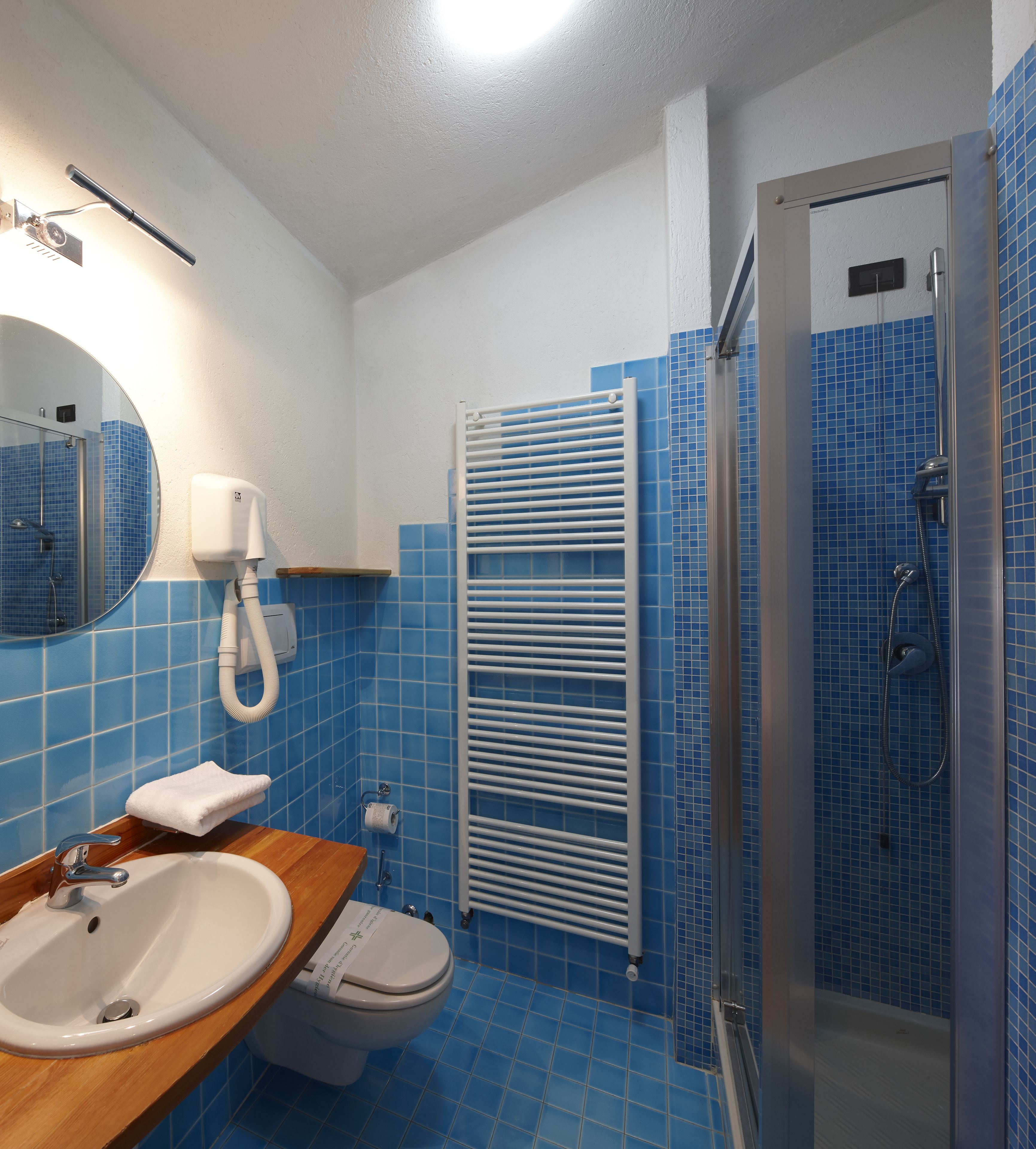 Un baño con lavamanos blanco, inodoro, ducha con puerta de cristal y toallero.