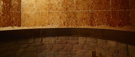 A stone fireplace with a brick hearth, a wooden bench, and a stone wall.