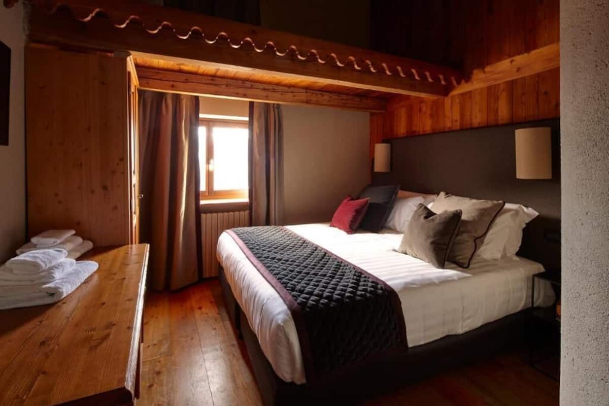 A wooden-paneled bedroom with a bed, a wooden bench with towels, and a window with curtains.