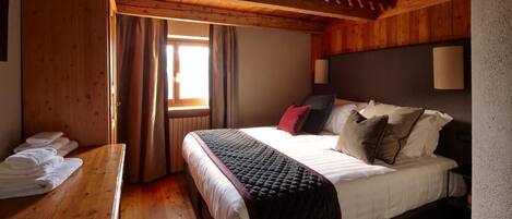 A wooden-paneled bedroom with a bed, a wooden bench with towels, and a window with curtains.