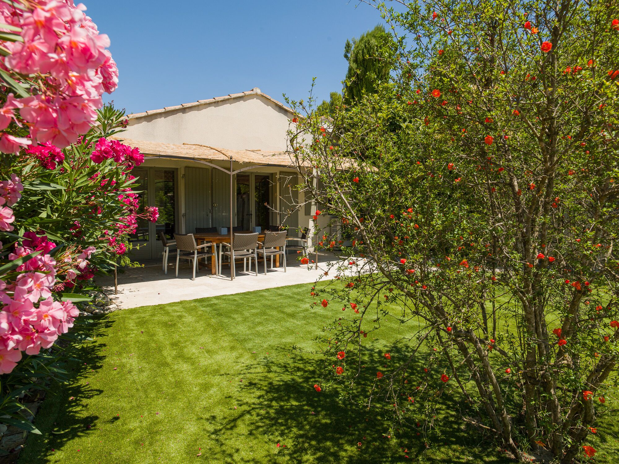 A house with a covered patio, a lawn, and flowering plants.