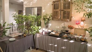 A dining area with tables covered in tablecloths, surrounded by potted plants and a mirror on the wall. - Hotel de Charme L'Amandière (St.-Rémy-de-Provence)