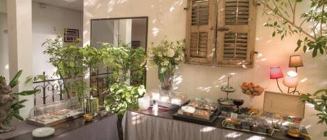 A dining area with tables covered in tablecloths, surrounded by potted plants and a mirror on the wall.