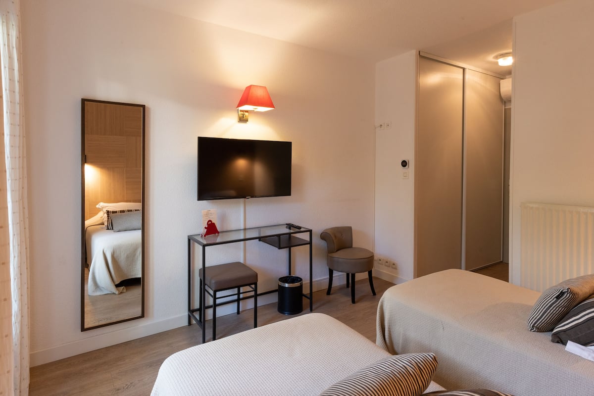 A hotel room with two beds, a desk with a chair, a TV mounted on the wall, and a wardrobe.