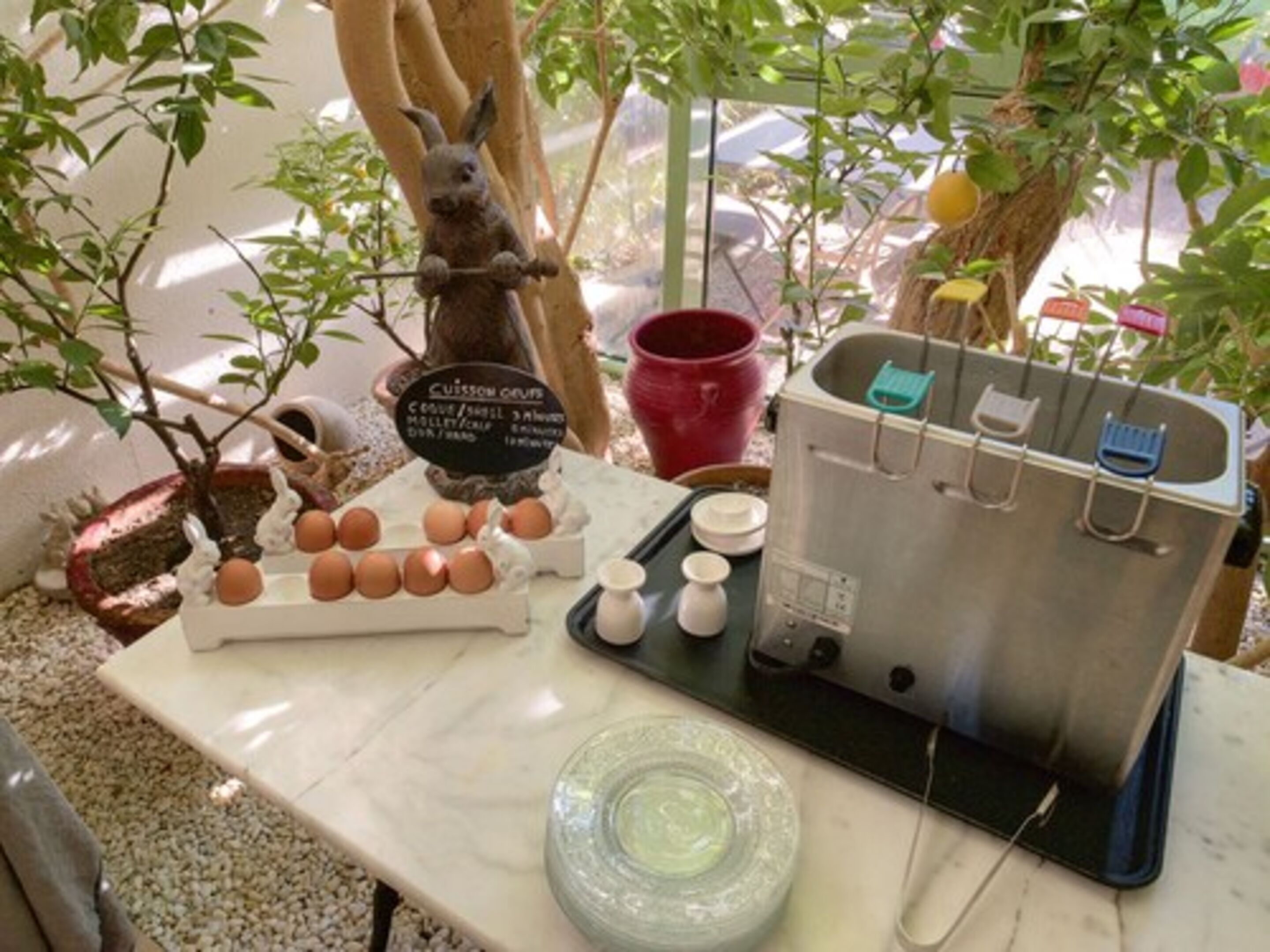 A kitchen setup with a rabbit figurine, eggs, a coffee maker, and a kettle on a marble countertop.