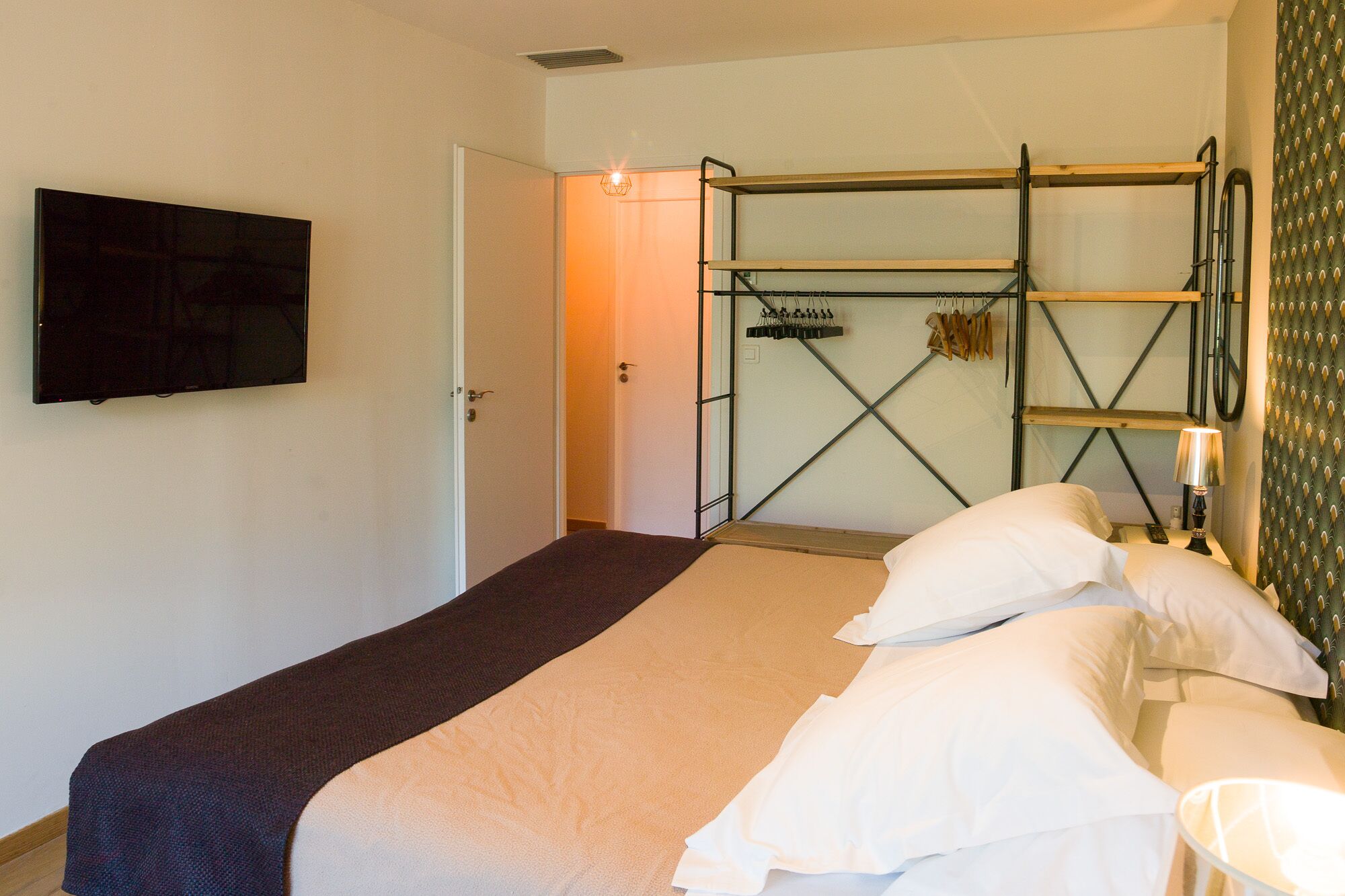 Een slaapkamer met een bed, een aan de muur bevestigde televisie en een deur die naar een andere kamer leidt.