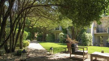 A garden pathway leading to a seating area with a bench and table, surrounded by trees and greenery.