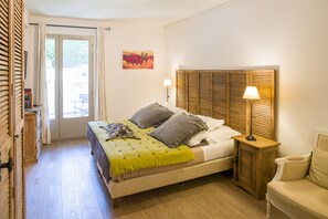 A bedroom with a bed, bedside lamps, a wooden headboard, a sofa, and a painting on the wall. - Hotel de Charme L'Amandière (St.-Rémy-de-Provence)