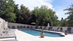 A swimming pool with lounge chairs and umbrellas, surrounded by trees and a clear sky. - Hotel de Charme L'Amandière (St.-Rémy-de-Provence)