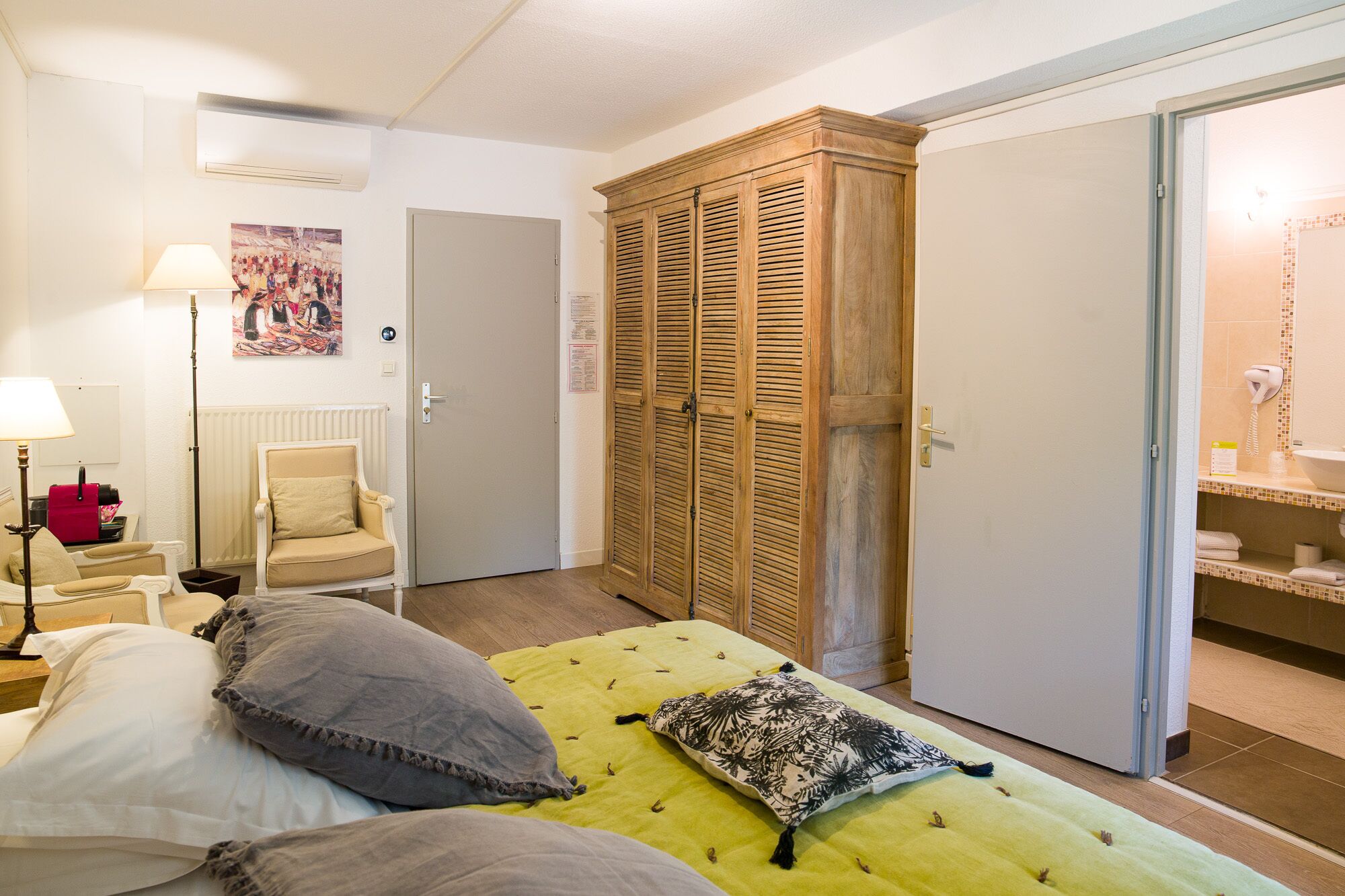 Habitación de hotel con cama, una silla, armario y baño visible a través de una puerta abierta.