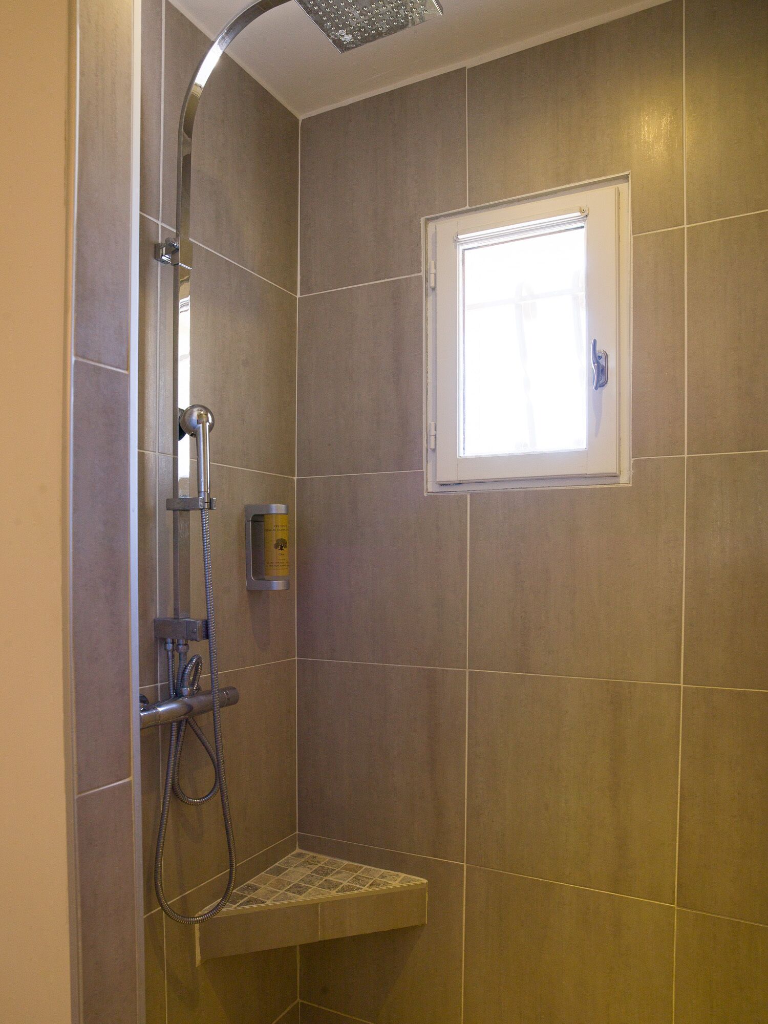 A shower with a handheld showerhead, a handheld shower attachment, and a small shelf with a bottle.