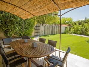 A covered patio with a wooden table and chairs, surrounded by lush greenery and a wooden fence. - Hotel de Charme L'Amandière (St.-Rémy-de-Provence)