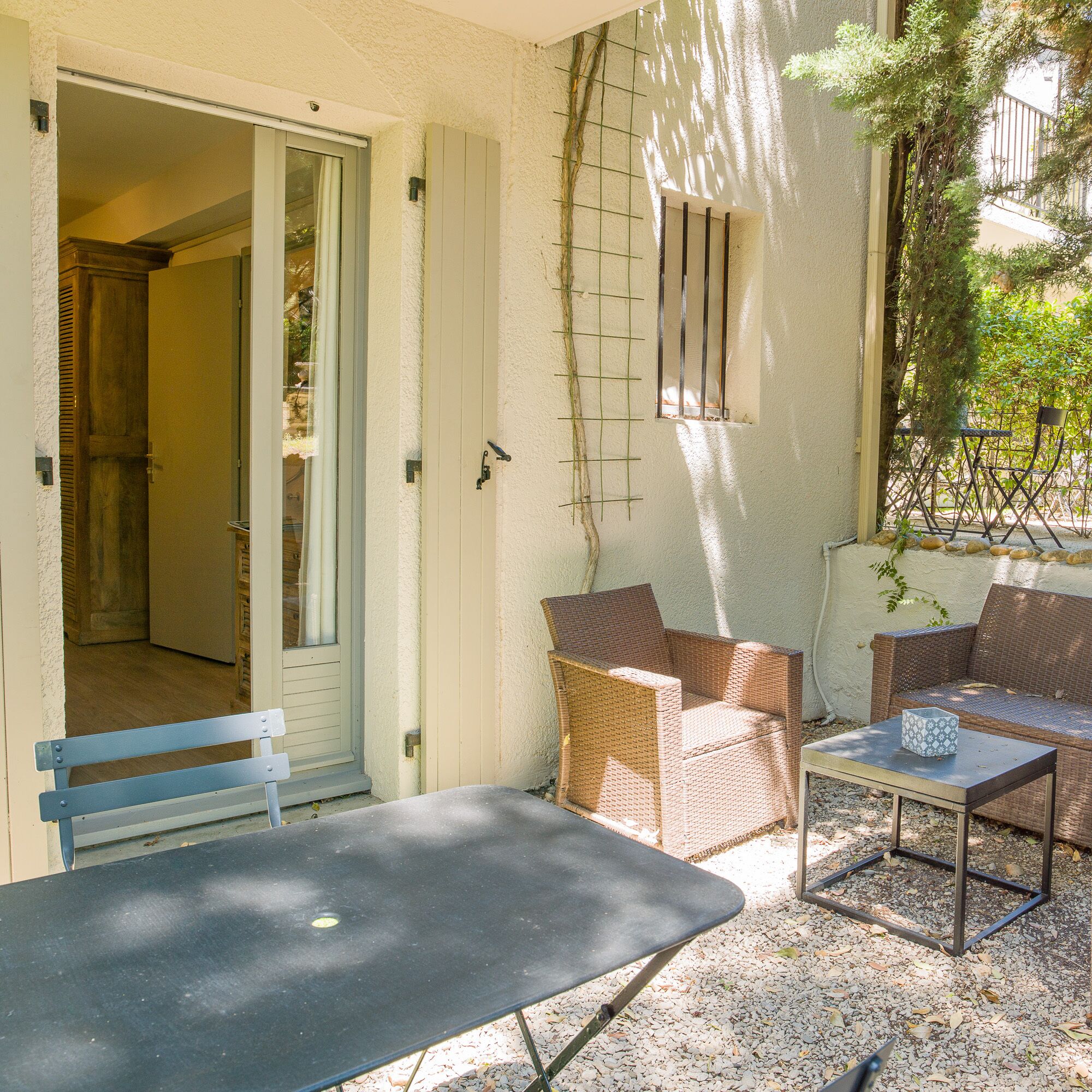 Un patio exterior con una mesa, dos sillas de mimbre y un banco.