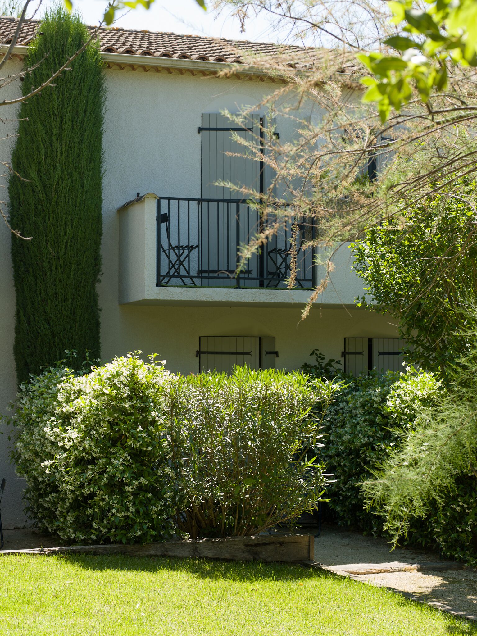 A two-story building with a balcony, a tall green hedge, and a well-maintained garden.