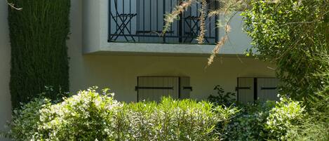 A two-story building with a balcony, a tall green hedge, and a well-maintained garden.