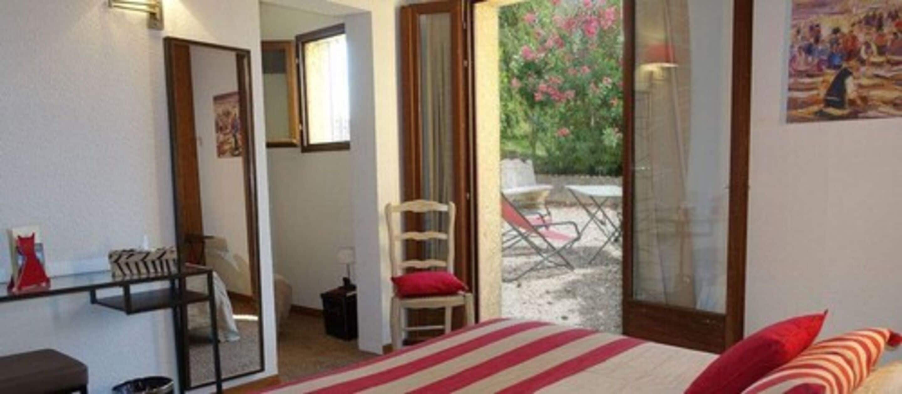 A bedroom with a bed, a chair, a desk, and a view through a glass door to an outdoor area with a chair and table.