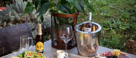 An outdoor dining setup with a pizza, salad, cheese platter, and drinks on a table.